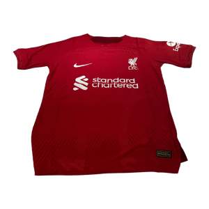 En Liverpool tröja i storlek s som är röd. Den är perfekt passande och av hög kvalitet. Dess andningsförmåga gör den idealisk för både matcher och träning.