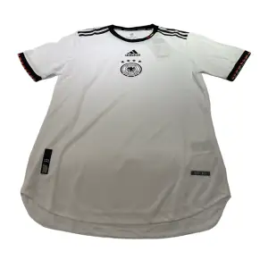 En Tyskland tröja i storlek M som är vit. Den är perfekt passande och av hög kvalitet. Dess andningsförmåga gör den idealisk för både matcher och träning.
