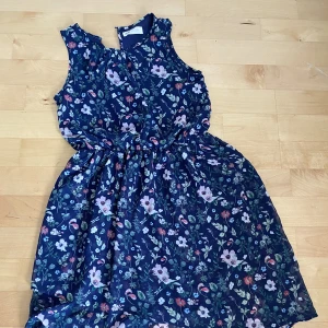 Blommig Klänning barn  - Klänning i bra skick. Den är längre bak en fram. 