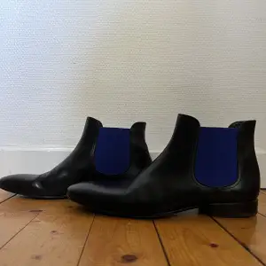 Knappt använda Pete Sorensen Phantom svart & blå skor i storlek 44. Väldigt bra skick. Handgjorda Chelsea boots tillverkad av ett enda läderstycke. Lätt och smidig italienskt kalvläder. Säljs nya av Pete Sorensen för 4450sek (380€). 
