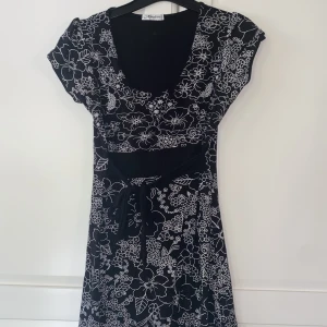 Svart klänning med blommor - Svart klänning med vita blommor och ett band för att knyta i midjan. Storlek 40 men passar XS & S