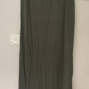 Olivgrön kjol från Vila. Storlek L. Resår i midjan och strechigt material.  Längd ca 93 cm. En slits på ca 35 cm på ena sidan.