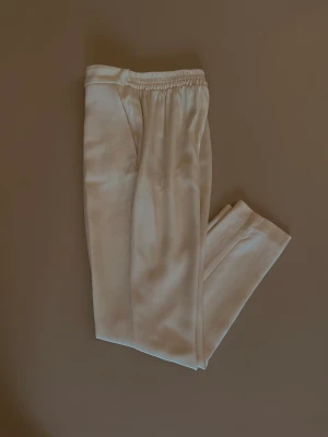 Upcycled Designer Silk Pant - Silk Pleated Front Dress Pant with 2 Pockets. Tapered leg for slimming effect. Elastic waistband.   Waist to inseam is 26CM. Made with Deadstock Designer Silk Fabric. Excellent Condition.  92 CM Length 64 CM Waist 80 CM Hips 66 CM Inseam