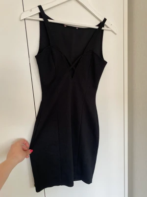 Klänning  - Snygg festklänning i svart med lite textur i tyget. Storlek 38 tajt med ett ”nyckelhål” i urringningen. Hel och nytvättad. Etiketten är bortklippt. 