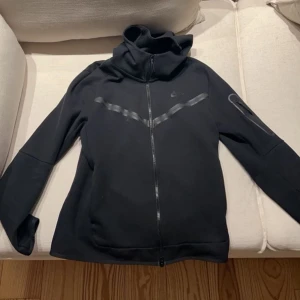 Svart Nike tech - Tja! Säljer nu en fet Nike tech då ja inte längre använder den. Tröjan är i mycket bra skick och använts sparsamt. Skriv vid önskan av fler bilder. Hör av dig vid frågor!