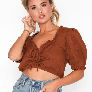 Oanvänd Topp från Nelly - Oanvänd topp från Nelly trend i storlek 36. Knappar bak, går att knyta/dra åt fram, puffärmar och volang, rostfärgad. Super fin🧡