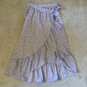 Lila blommig midikjol från monki  - Super söt midi kjol från monki, omlott design, lila blommig, finns knapp samt knyts i midjan, nyskick