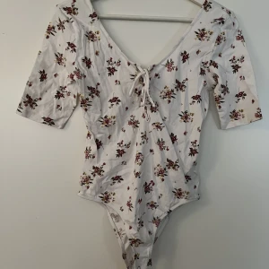Blommig body - Jättefin blommig body. Sparsamt använd. Har en liten snörning som man kan välja att antingen ha på framsidan eller baksidan.