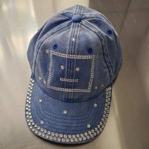 New Acne Studios cap in blue and with silver stones embellishments. The lagom face on front. One stone is loose, but there are extra silver stones in the hangtag. Can send more photos. 100% new condition. Can be slightly flexible with the price :)