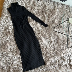 Klänning - Lång klänning med mindre slits och hög hals. Använd 1 gång. Fint skick. Sitter inte tight i halsen. Stlr. XS men mkt stretchigt material. Tappar inte formen i tyget.  