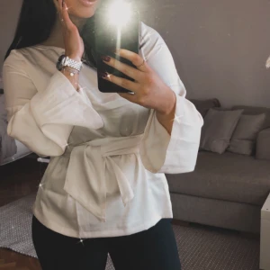 Blus från bubbleroom - En beige blus från bubbleroom med långt brett band i midjan, som jag även kunnat använda som fin scarf  runt halsen.   Använd 2 ggr.  Storlek 36