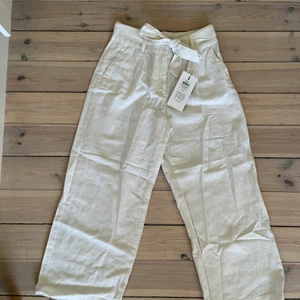 Vita linnebyxor - Vita linnebyxor i croppad modell med knytning i midjan! High waist, storlek XS men passar även S. Helt oanvända med lappen kvar. Köpta för 399 men säljer då jag tyvärr är lite för lång (172 cm)