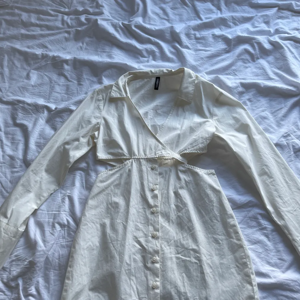 Säljer nu min vita skjortklänning då den blivit för liten. Väldigt charmig modell på den. Knappar fram och sen knyter man den i bysten för att få fram en form. Den har även vita på sidan för att framhäva lite. Passar till både fest och vardag!. Klänningar.