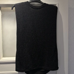 Glitter topp - Svart glittrig topp med axelvaddar från Ellos. Strolek 34/36