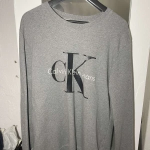 Calvin Klein tröja - Jättefin grå Calvin Klein tröja med tryck storlek L. Inte mycket använd, väldigt fint skick. Nypris ca 1000kr