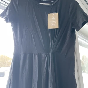 Lång klänning - Fin lång svart klänning med knytdetalj vid midjan.  Använd 0 gånger, lapp sitter fortfarande kvar. Från rök och djurfritt hem.