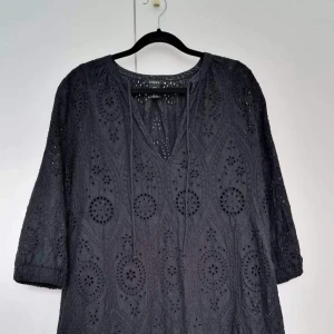 Klänning  - Storlek S Denna svarta tunika med härlig vidd och volang har ett genomgående spetsmönster i 100% bomull. Ca 80 cm  Sparsamt använd, inga anmärkningar. Pris 180:- 