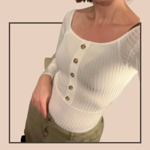 NY! Långärmad body med knappar från Boohoo  - Helt ny långärmad ribbad vit body, träfärgade knappar. Lapparna kvar.  Söm som markerar midjan gör den extra snygg till t.ex. höga jeans. Perfekta toppen för en vårig look! Strl 36 Material: 95% polyester, 5% elastan  Inga defekter, endast provad.