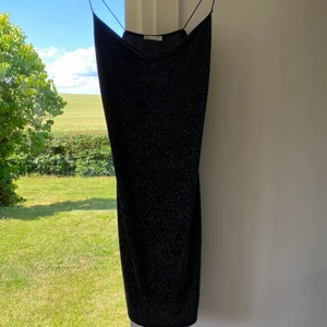 Festklänning från Nelly - Svart klänning med silvrigt glitter i ”vattenfallsmodell” upptill! Lätt material som formar sig så fint efter kroppen, perfekt till fest! 