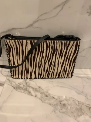 Axelremsväska från Zara - Snygg axelremsväska från zara i äkta läder med snygga detaljer. Kan användas som axelremsväska eller kuvert. ”Hårig framsida” med back i svart läder.  Superfint skick!  Rök och djurfritt hem.