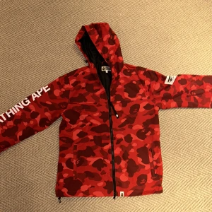 A Bathing Ape röd camojacka  - Säljer min Bathing Ape camojacka. Fantastiskt skick, knappt använd och ser helt ny ut. Den var designat för herr men kan också funka för Unisex.