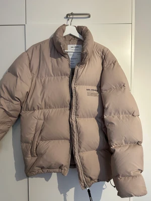 Dunjacka, Axel Arigato - Beige dunjacka från 21/22-kollektionen. Välanvänd med lite få skavanker på arm och krage, annars fint skick, inget trasigt. Stl M. Ord pris 3499kr.