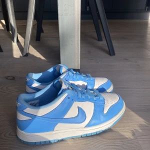 Nike Dunks ”unc” low - Säljer dessa riktigt snygga blå Nike dunks ”unc” low som är använd fåtal gånger och är därmed i väldigt bra skick! Säljer då de inte är min stil längre. Köptes nya för ca 3000 kr!💙 Vid många intressen startas en budgivning!🫶
