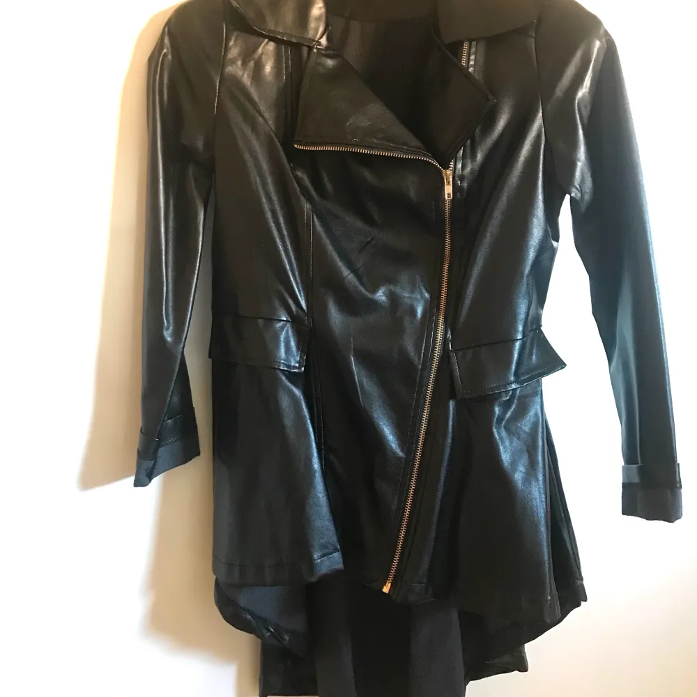 Asymmetrisk jacka i faux leather. Längd fram vid blixtlås 60cm, baksidan 97cm.. Jackor.