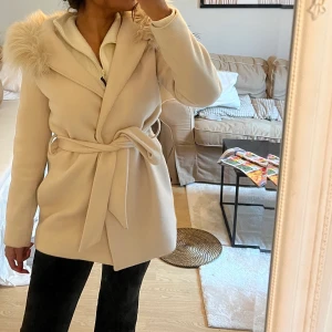 Kort beige kappa - En perfekt kappa med perfekt längd som funkar till allt, bra skick, knyter runt midjan, man kan ta bort pälskragen på luvan vilket jag föredrar (se sista bilden) 