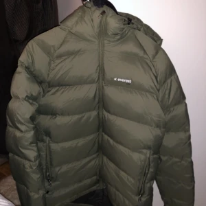 Dunjacka Everest  - Perfekt vinterjacka! Militärgrön dunjacka/puffer från Everest. Passar mig som är M. Köpt begagnad och tidigare skador finns på ärmen, se bild 3, därav priset. Kan försöka laga det/sy innan jag skickar om så önskas. Frakt ingår 🤠
