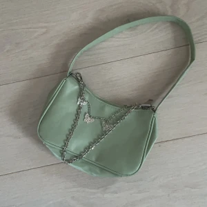 Trendig handväska i pastellgrönt - Snygg och trendig väska med kedjor som man kan ta bort om man vill. Perfekt storlek för att ha med sig mobil och annat smått! Vet ej materialet, men inte skinn och i superfint skick! 