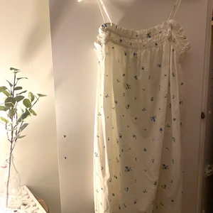 Kort sommarklänning  - En fin somrig klänning från H&M. Lite pösigare klänning. Vit med blåa blommor. Går strax över knäna för mig som är 172. Använd endast en gång. Bra skick! 