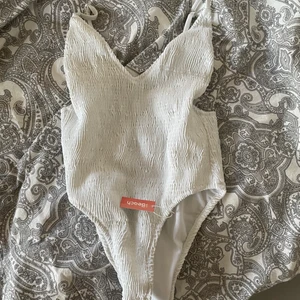 Vit baddräkt - Vit baddräkt från Nelly som är helt oanvänd. Den är öppen i ryggen och väldigt töjbar, inte genomskinlig alls. Passar både xs och s