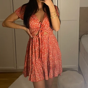 Blommig klänning - Blommig röd klänning. Med knyte framme vid brösten. Passar s/m