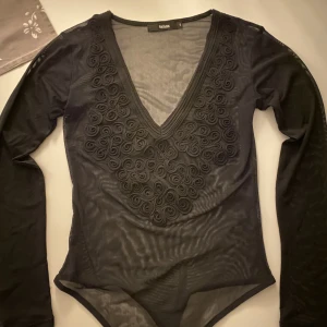 Body med dekor (strl. S) - En genomskinlig svart body köpt på BIKBOK i storlek S. Knappt använt och därför mycket bra skick, inga defekter. Mycket snygg och passar till fest! Nypris ca 200-300kr. Priset kan alltid diskuteras!