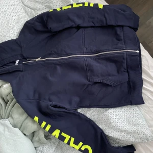 Säljer blå och gul Calvin Klein hoodie - Säljer nu min blåa Calvin Klein hoodie med drag kedja med gul text för att den inte kommer till användning längre tyvärr, använd några gånger, fint skick!💗