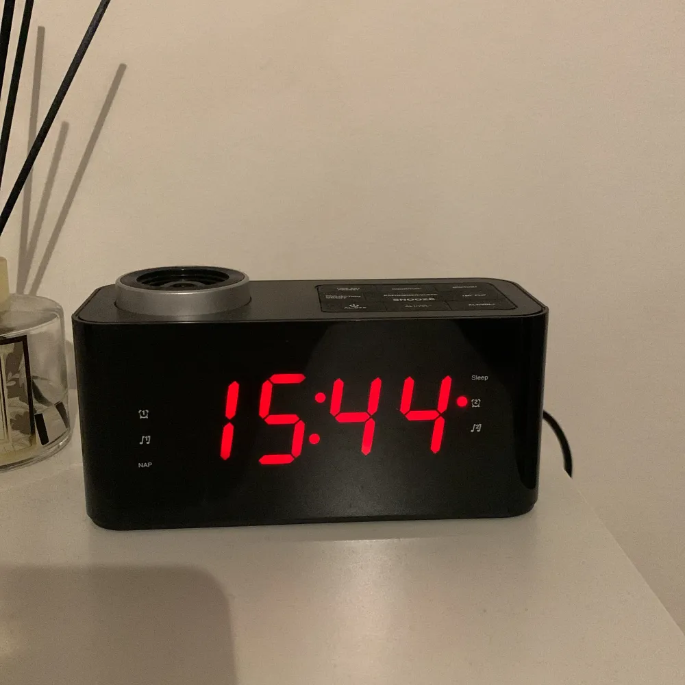 Dröjer denna efter som jag inte använder den. Den lyser upp i taket eller på väggen, den har en radio, man kan starta larm på den , och den drivs inte av batterier utan eluttag . Muu.