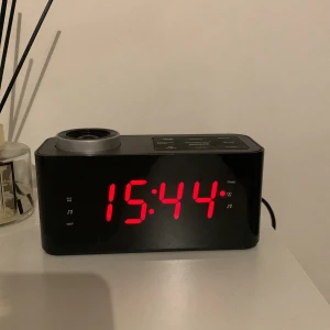 Projektor klocka  - Dröjer denna efter som jag inte använder den. Den lyser upp i taket eller på väggen, den har en radio, man kan starta larm på den , och den drivs inte av batterier utan eluttag 