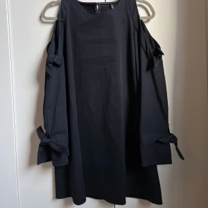 Zara marinblå klänning i tjockt tyg - Sparsamt använd klänning från Zara i tjockt tyg och kvalitativ känsla. Den är kort och har ”bara” axlar och knytdetaljer vid axlarna och på ärmarna. Kände mig så fin när jag har hade den på ett dop!