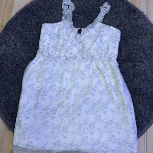 Blommig blus/klänning - En fin blommig blus/klänning i färgerna lila, rosa och blå. Veckade band där uppe. Använd några gånger. Fint skick, i storlek s/m. Kan inte se märket på känningen tyvärr.