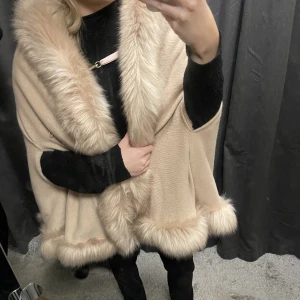 kape/poncho - Säljer denna kape/ poncho, den är köpt i butik i stockholm för några år sedan men nu säljer jag den för jag inte får någon användning utav den. den är beige med rosa foder innanför och en pälskrage på. den är varm och snygg att slänga på sig:)