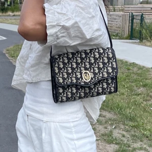 Vintage Christian dior  - Äkta Dior handväska  Monogramcanvas med detaljer av skinn och guldfärgad metall. Märkt Christian dior, made in France. 1970/80-tal. Höjd ca 16 cm, bredd 21,5 cm.  Den är i bra skick. Den kan justeras så att bandet blir kortare/längre. 