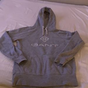 Gant  - Grå gant tröja med ett vit stort tryck på framsidan av tröjan i mitten där det står ” GANT” 