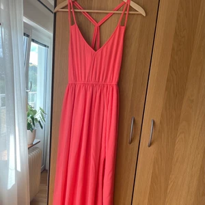 Festklänning i fin persikafärg  - Lång festklänning med slits på vänster ben. Fin persikafärg med tylltyg vilket ger en elegant känsla. Ryggen är öppen delvis och framsidan är v-ringad. Använd en gång. Storlek S.