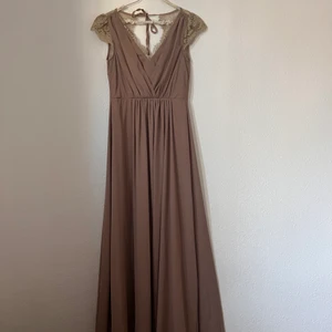 Oanvänd By Malina Klänning! - Fin maxiklänning från By Malina. Den snäva midjan och den draperade fronten gör den smickrande för de flesta figurer. Spetsdetaljerna ger klänningen en söt-fakor som är on point. V-ringningen fram och bak är snitt som ger den där extra moderna touchen.  Tillverkad av: 100 % polyester. Tvätt: Handtvätt. Färg: GOLDEN BEIGE.          