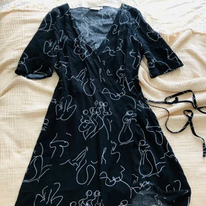 Söt omlottklänning  - Omlottklänning från NA-KD använd fåtal gånger! Mönster av kroppar i vita linjer. Frakt ingår i priset! Står strlk 34 men eftersom den är omlott så passar den på mig (som är mer en 36/38 numera) och säkert på större storlekar.