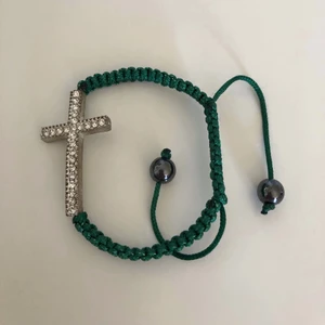 Armband med kors - Armband med ett kors, korset har rhinestones. Aldrig använt. Man justerar storleken med snörena