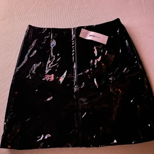 Kort kjol Ginatricot storlek 38 - Svart lackkjol. Låg i midjan. Aldrig använd.