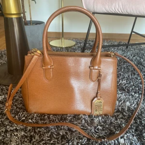 Väska Ralph Lauren - Använd men i bra skick.  Ena magneten för att stänga väskan har lossnat och limmats fast. Fungerar bra.