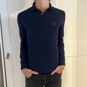 Långärmad Ralph Lauren piké  - Långärmad Ralph Lauren piké i färgen mörkblå. Inga defekter på tröjan. Size XS (slim fit) men lutar mer åt S. Modellen är 177cm. Hör av dig vid funderingar!